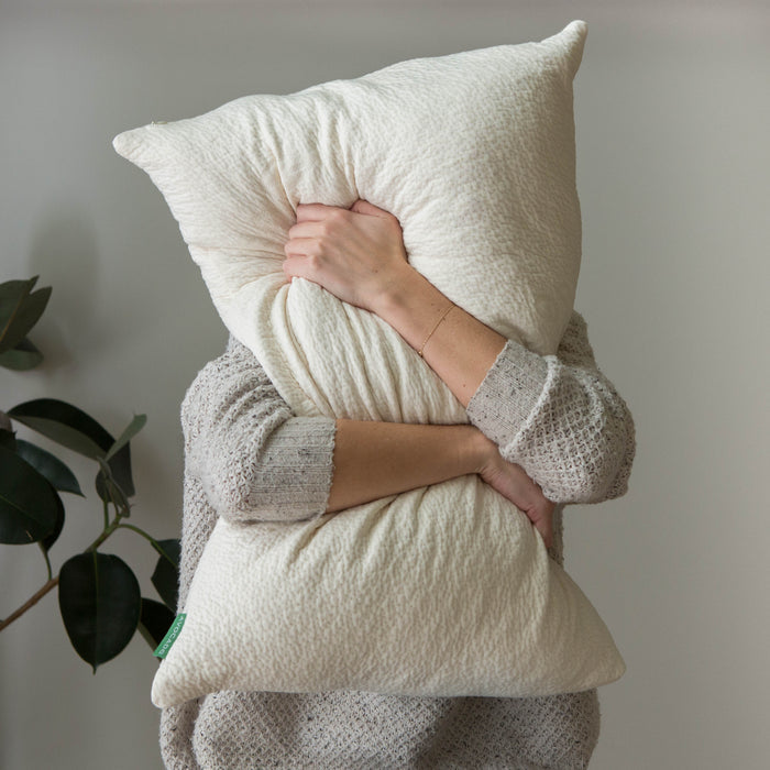 Textured off-white throw pillow with green brand label
