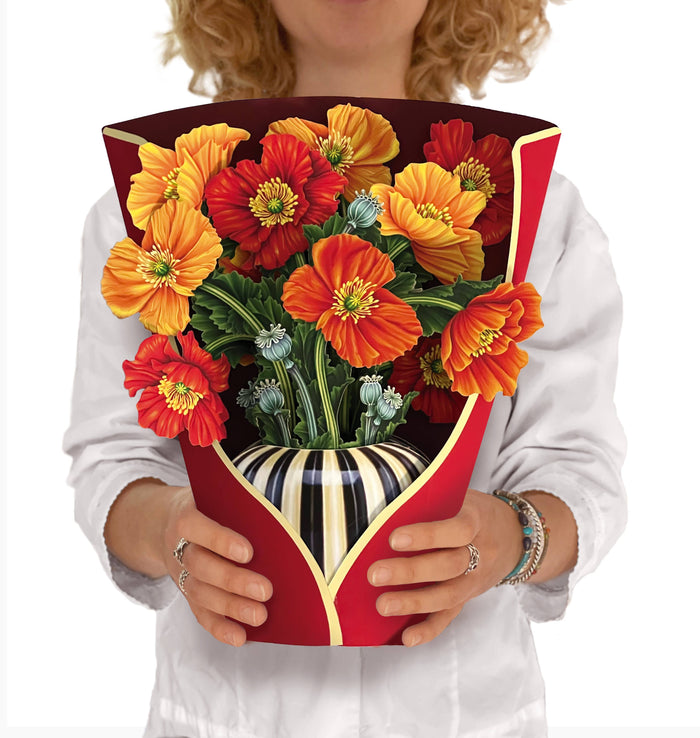 A person holding a pop-up greeting card with an arrangement of artificial French Poppies in a striped vessel.