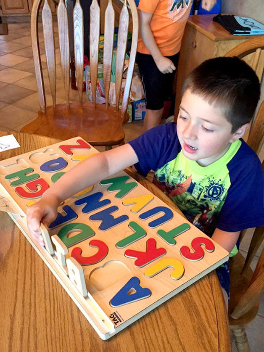 Child sitting at a table placing letters into a colorful wooden alphabet puzzle board.