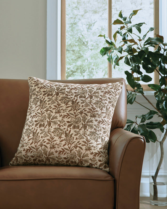 Square patterned throw pillow with brown leafy design on a tan fabric cover.