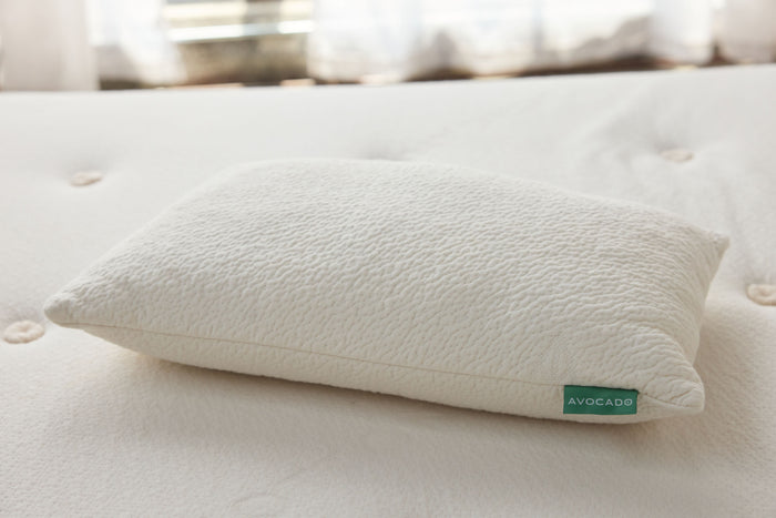 Off-white throw pillow on bed with green Avocado label