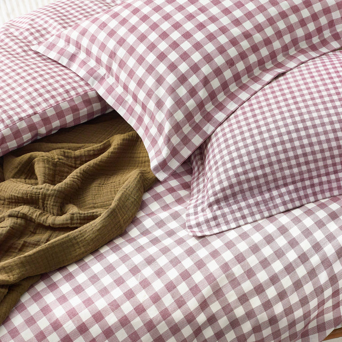 Berry and white checkered bedding with a brown blanket on a bed.