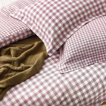 Berry and white checkered bedding with a brown blanket on a bed.