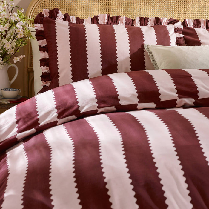 Striped bedspread with burgundy and blossom colors on a bed with pillows.