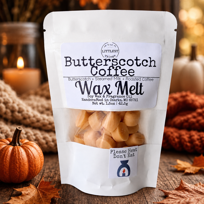 A white stand-up pouch of 'The Littlest Butterscotch Coffee' Wax Melt soy wax & fragrance oil, displayed on a rustic wooden surface with autumn leaves, a small orange pumpkin, and cozy background decor.