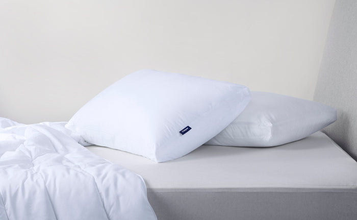Two white pillows with blue Casper logo tags resting on a bed.