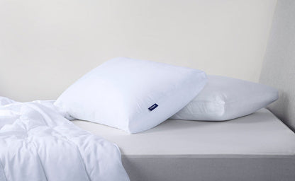 Two white pillows with blue Casper logo tags resting on a bed.