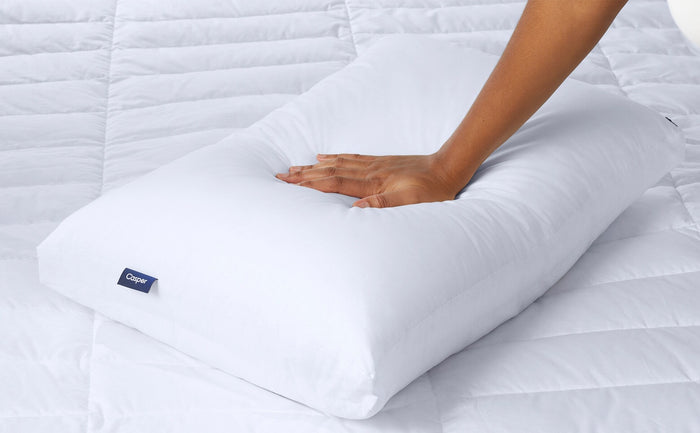 White pillow with blue Casper logo tag, close-up hands pressing on the surface.