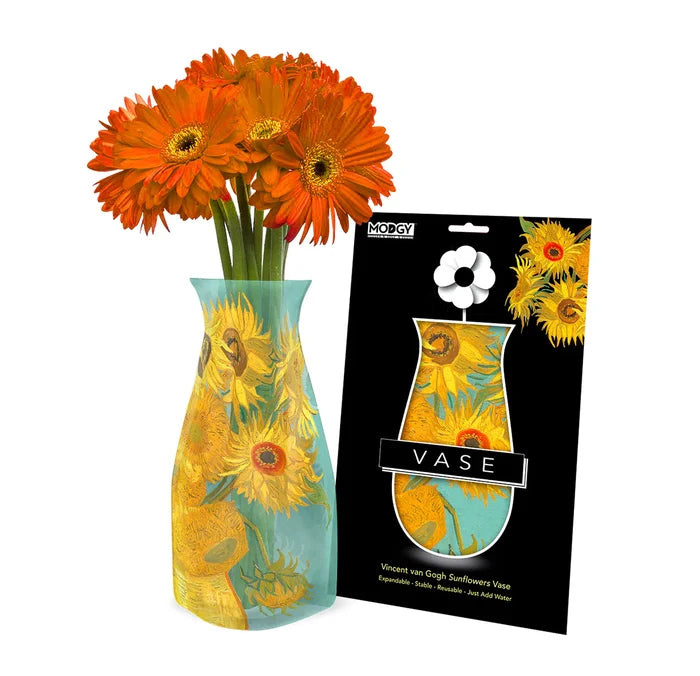 An expandable vase with a floral pattern, displayed alongside its packaging which also features floral designs. A bouquet of orange flowers is inserted into the vase.