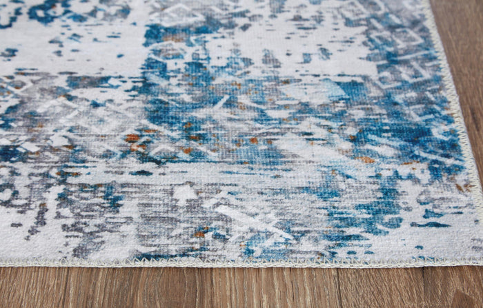 Blue-and-white abstract rug surface with distressed motifs near corner edge.