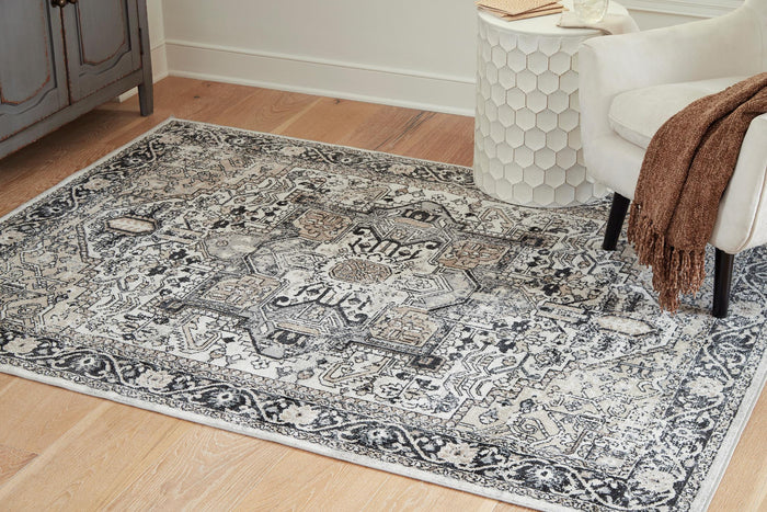 Light gray area rug with ornate geometric pattern, corner accents, flatweave look