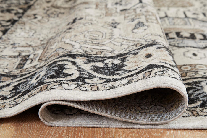 Rolled edge of light gray rug with black ornate pattern and low-pile texture