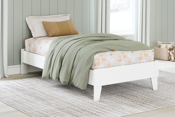 White platform bed styled with green blanket and patterned pillows