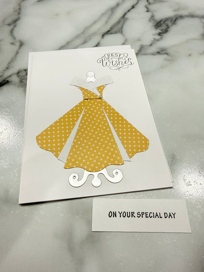 A white greeting card featuring a yellow and white polka dot dress illustration, placed on a gray marble surface next to a small white card that reads 'ON YOUR SPECIAL DAY'.