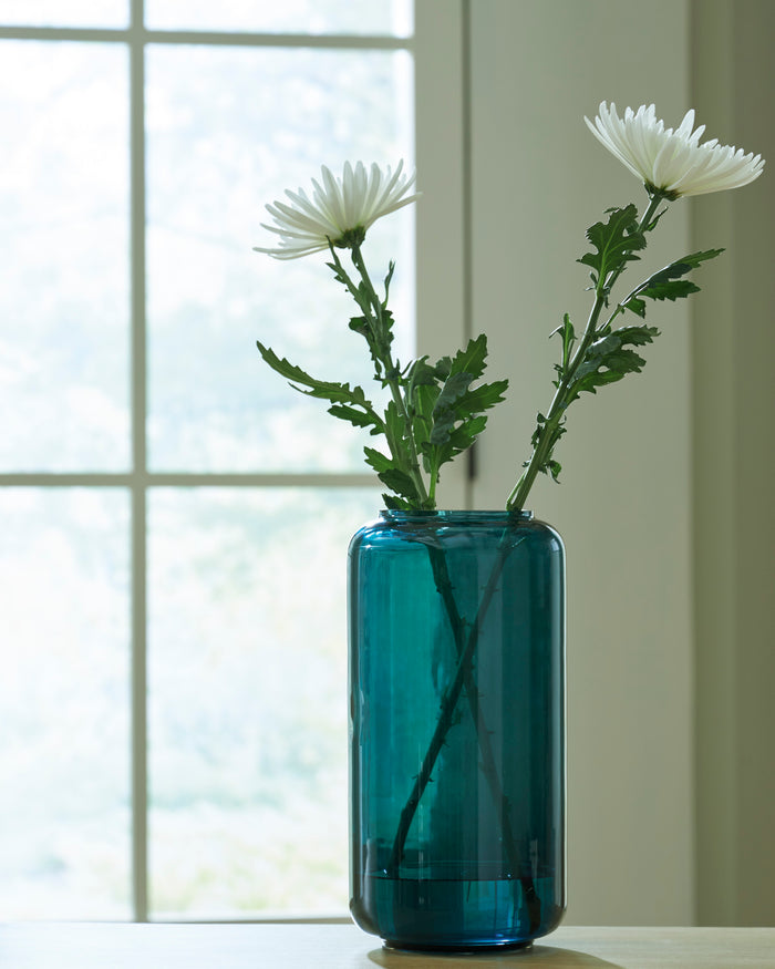 Teal glass vase with white daisies and green stems, tall cylindrical shape