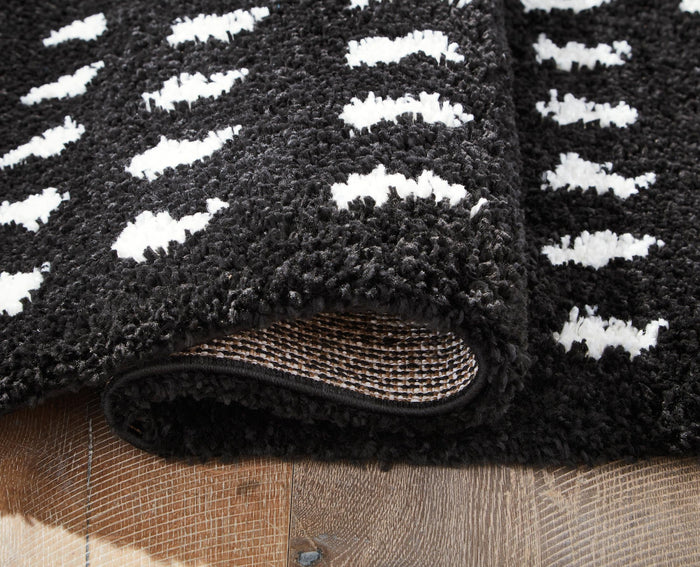 Black rug with white dash pattern and plush textured pile, close-up