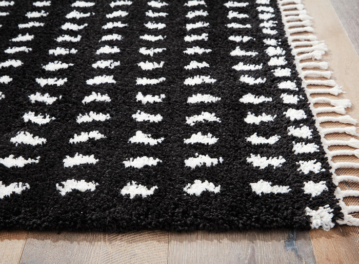 Black rug with white dash motif and cream fringed trim along the edge