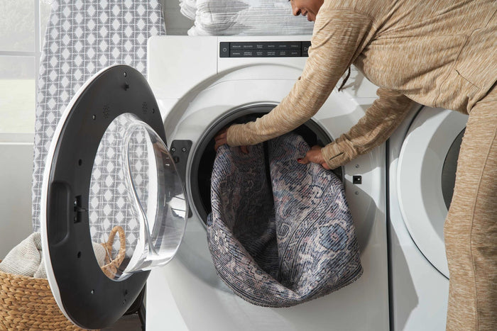 Person loading a blue and beige rug into a washing machine for washing