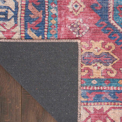 Washable rug corner with stitched edge in gray backing and red-blue pattern trim.