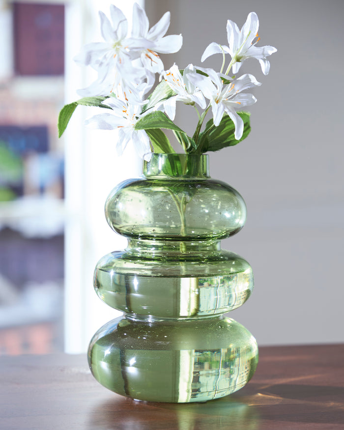 Green glass vase with stacked rounded shapes, holding white flowers and green leaves