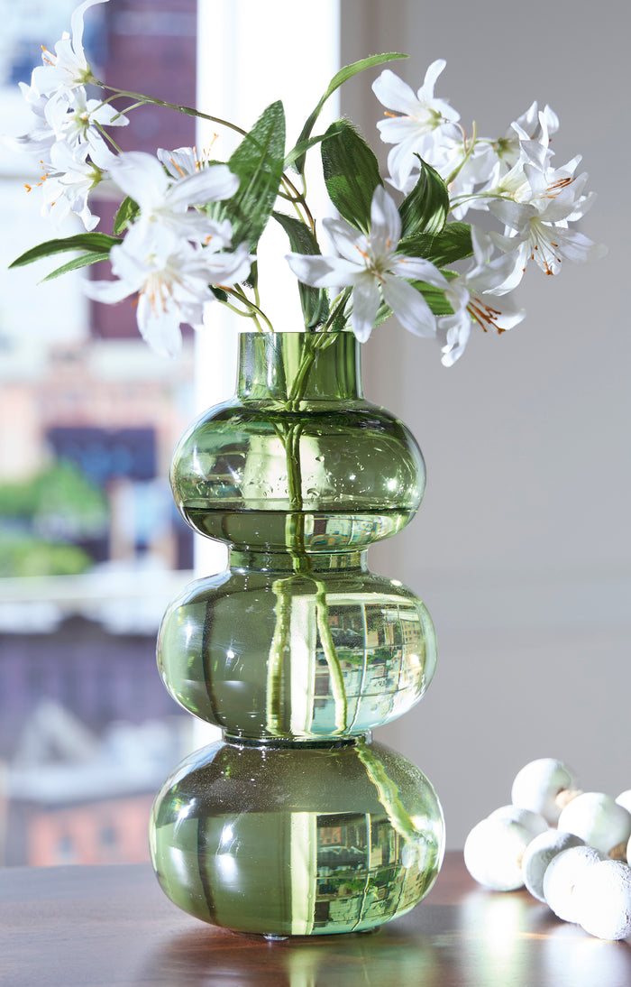Green glass vase with stacked rounded shapes, holding white blossoms and green stems