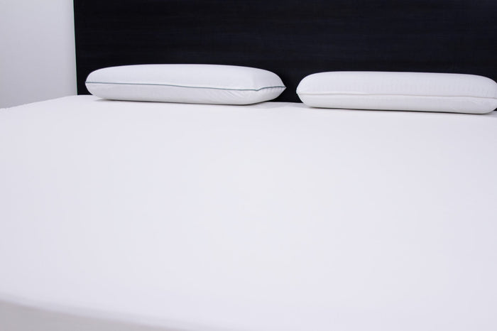 White mattress protector on bed surface with two white pillows in view