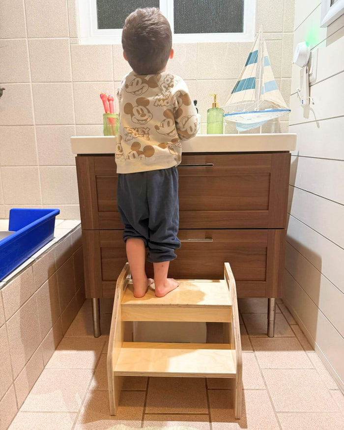 Child using a step stool to reach a sink in a bathroom