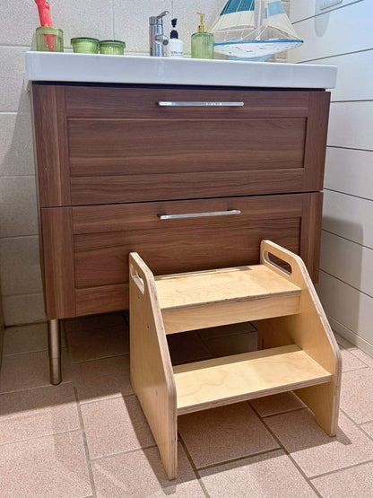 Wooden step stool in front of a wooden bathroom vanity with a white countertop.